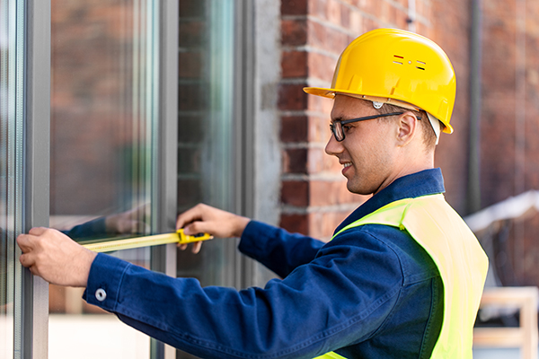 construction business and building concept — happy smiling male builder with ruler measuring window